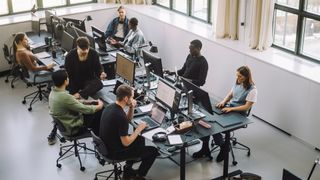 Tech workers sitting in an open plan office space using generative Ai tools on their desktop devices.