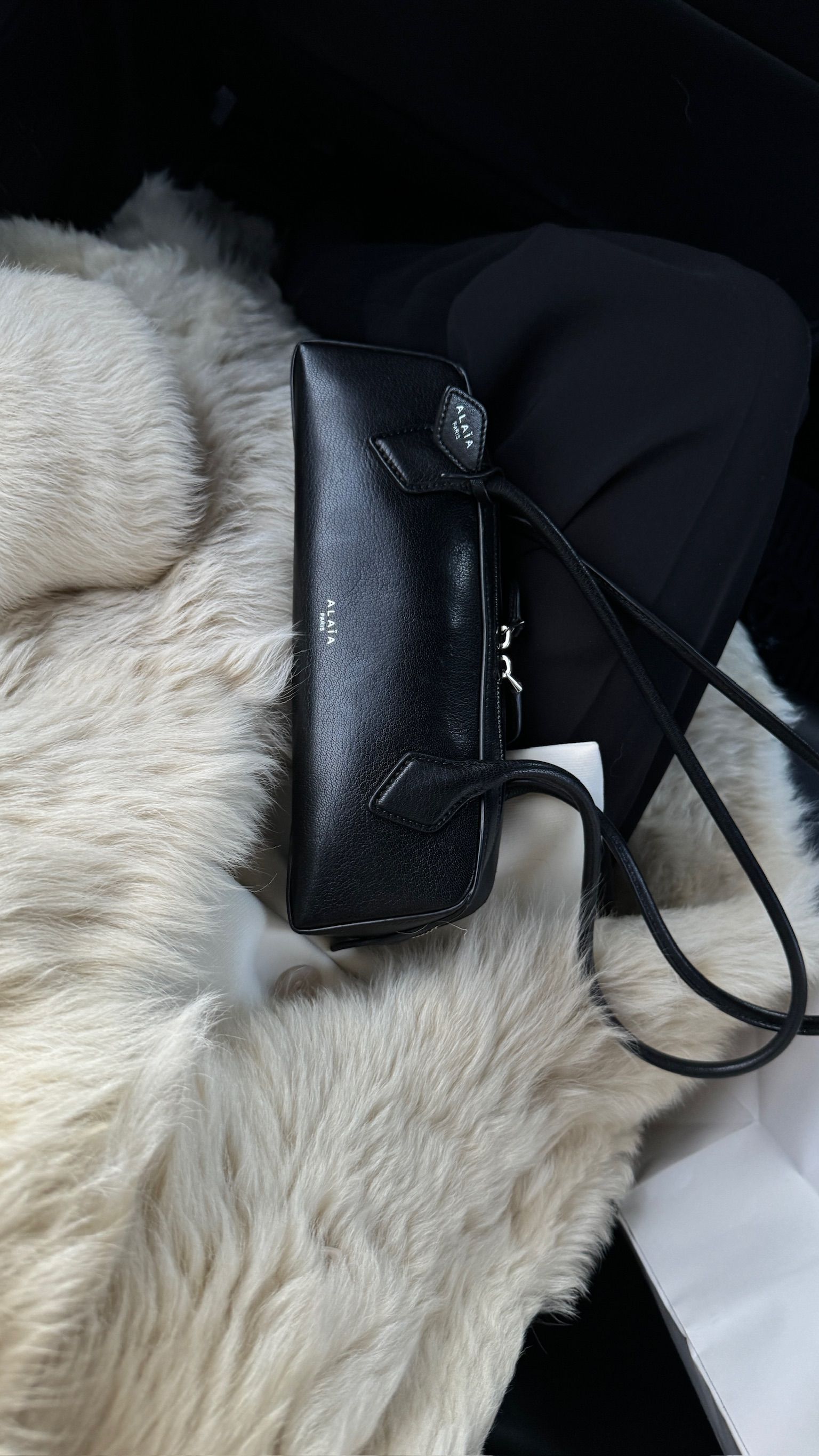 Caitlin Burke wearing an off-white shearling coat with an Ala&iuml;a Le Teckel Small Bag in black on her lap.