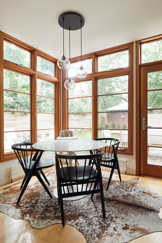 round dining table with black wooden chairs in corner with big windows and garden views and hide rug on wooden floor