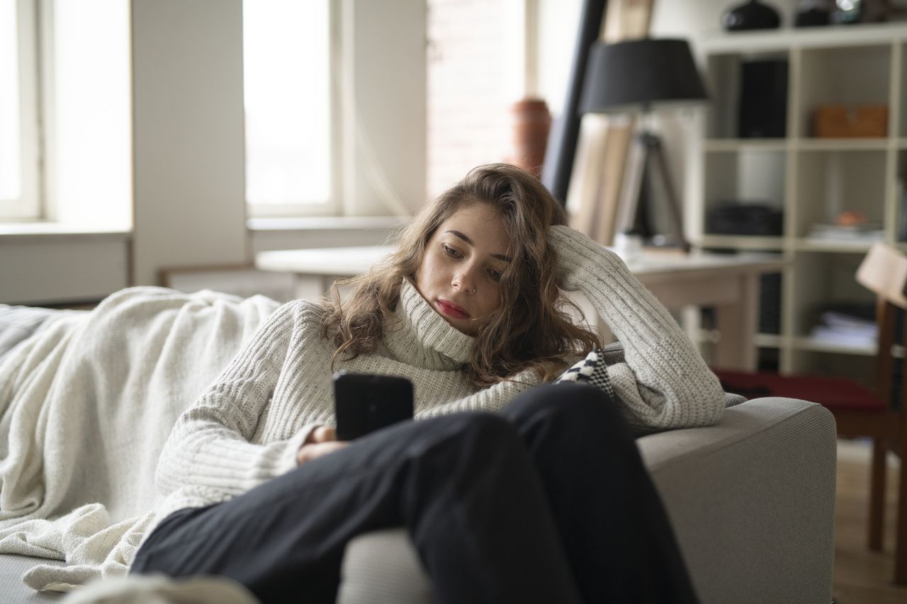 How to stop a phone addiction: A woman sits on her phone on her sofa at home