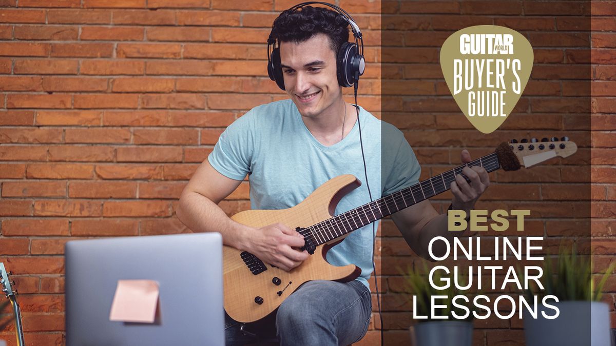 Man in blue t-shirt plays guitar in front of a laptop