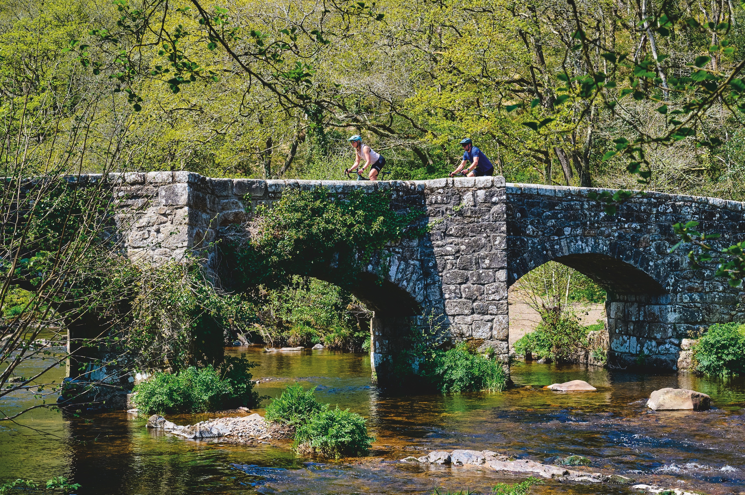 Two riders riding over a stone bridge