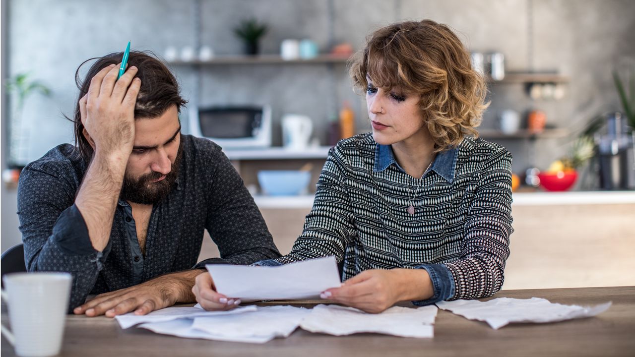 A stressed-looking couple who&#039;s getting a divorce go over papers including debt information.