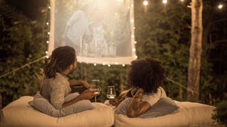 Outdoor projector in use in garden with couple laying on floor