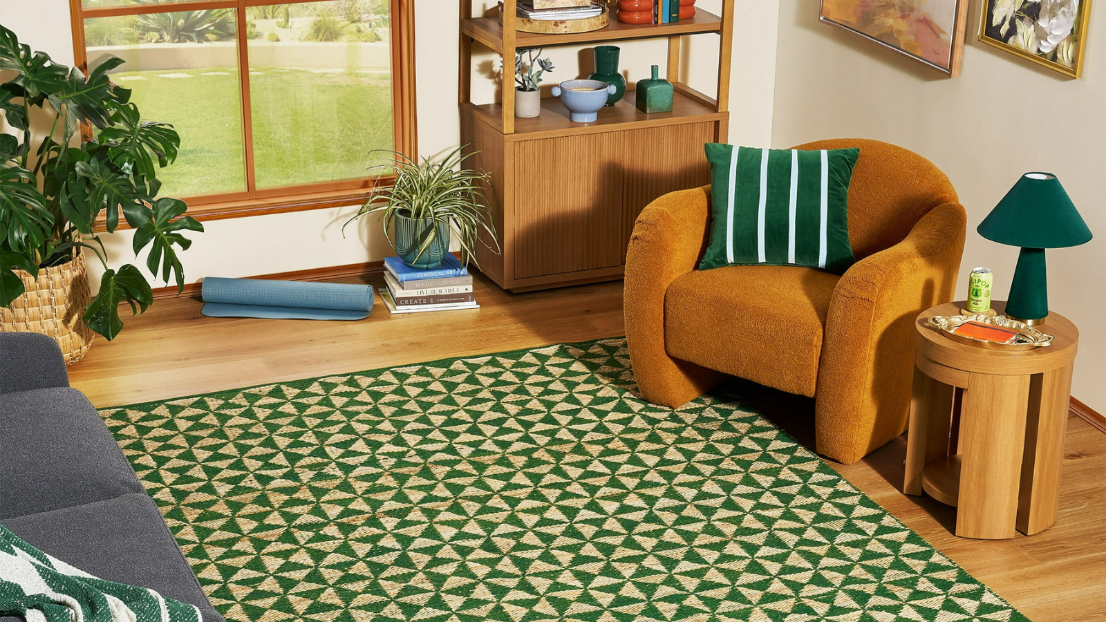 a living room with a green jute rug, an orange accent chair, a green and white striped pillow, a shelving unit with various decor, and a small side table with a lamp 