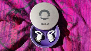 Ozlo Sleepbuds in an open case and on a purple pillow