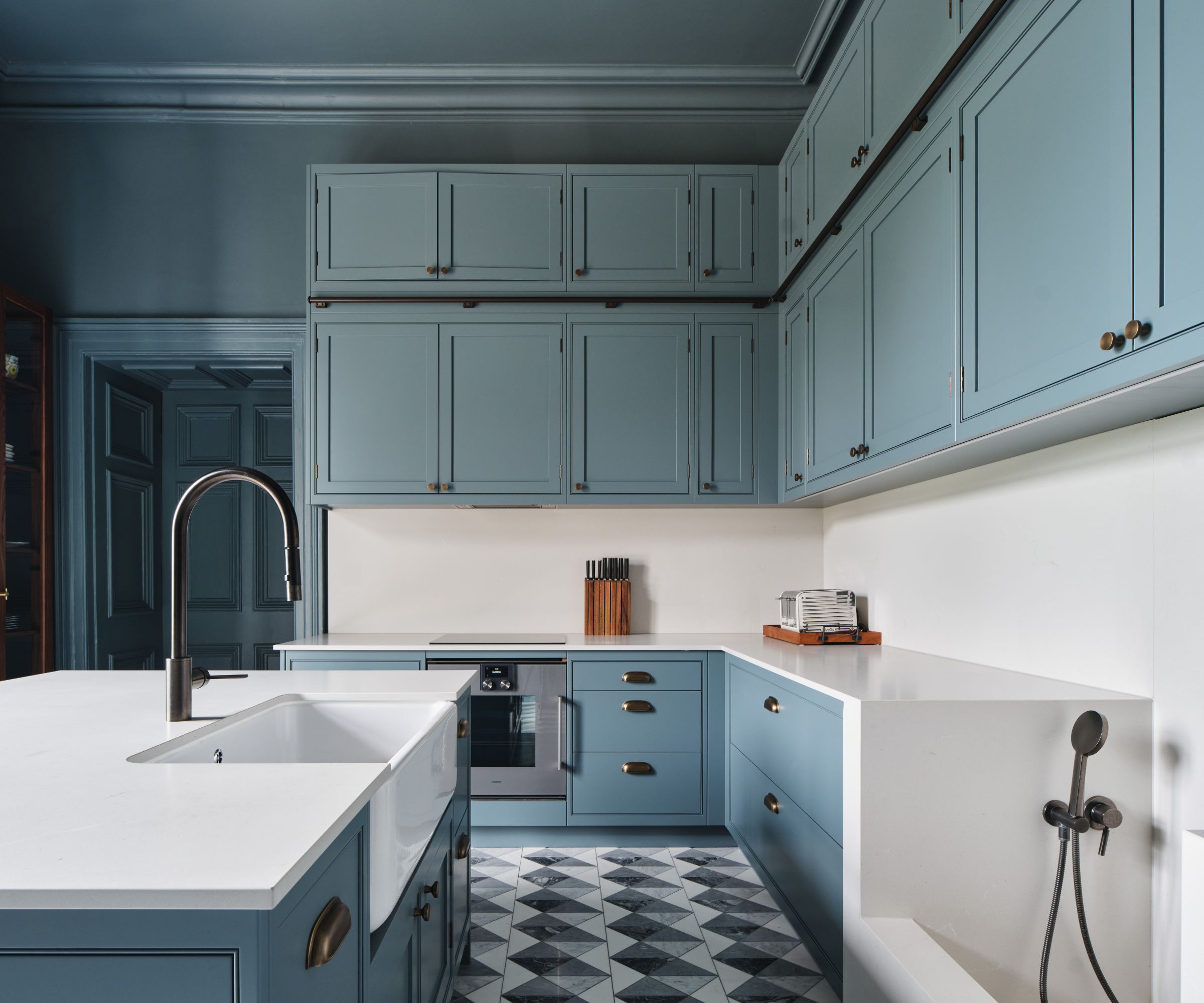A sleek utility room with blue shaker cabinets, monochrome geometric flooring, white worktops, and a built-in dog shower with black fixtures