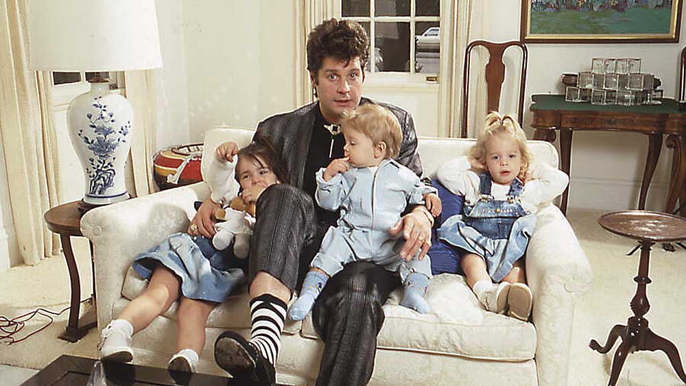 Ozzy Osbourne at home, sitting on the sofa with his three young children