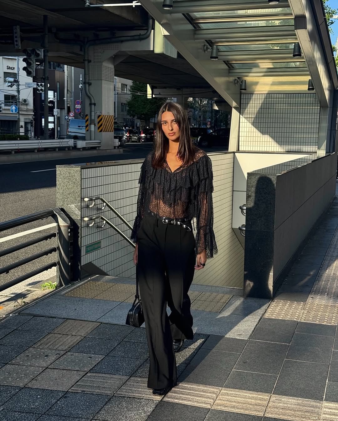 A woman wears black pants with a lace top and black patent leather loafers.