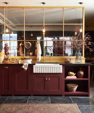 red burgundy kitchen with yellow painted interior window, slate gray floor tiles, rug, fluted sink, brass taps, lighting