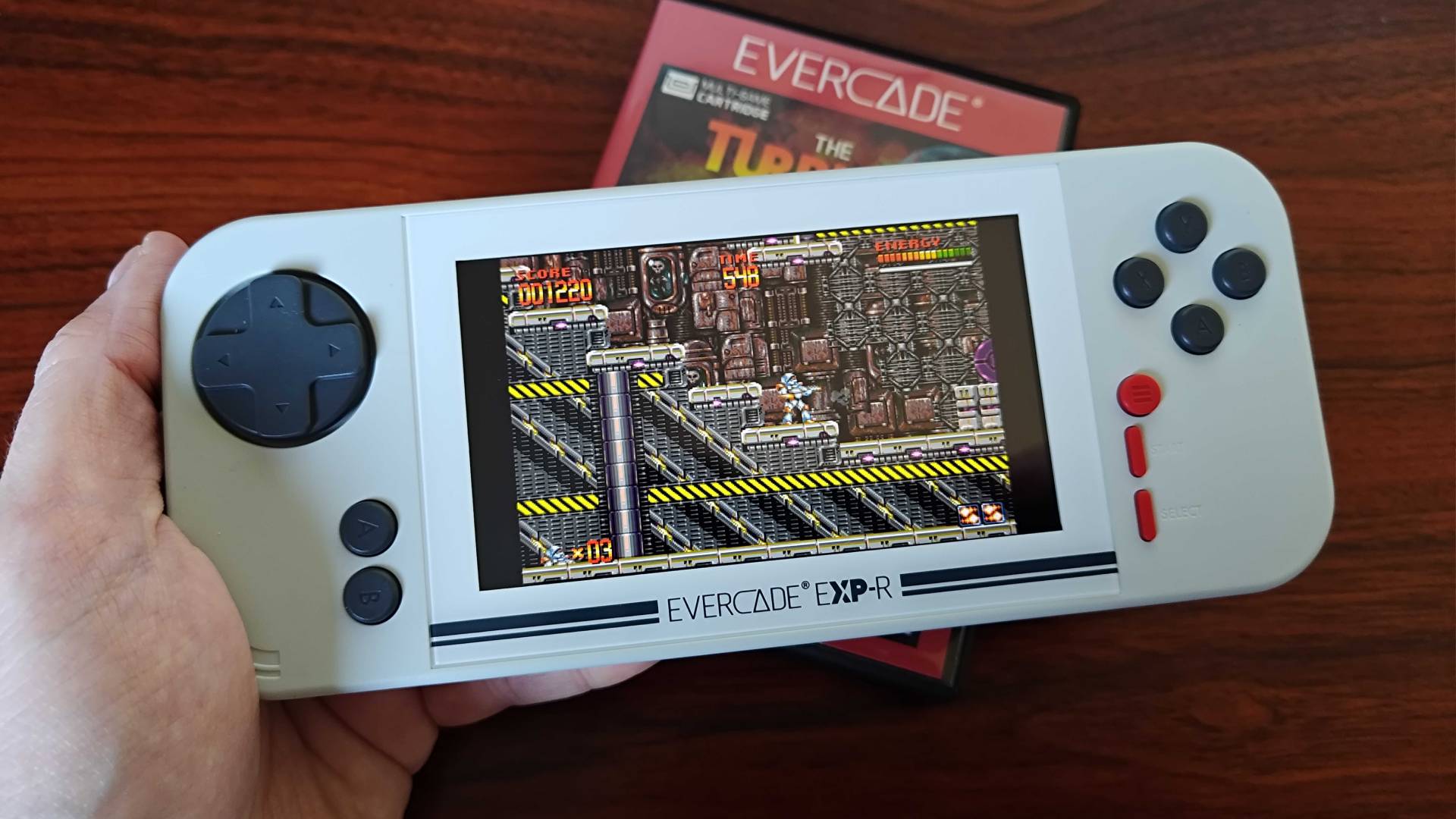Hand holding Evercade EXP with Mega Turrican gameplay on screen.