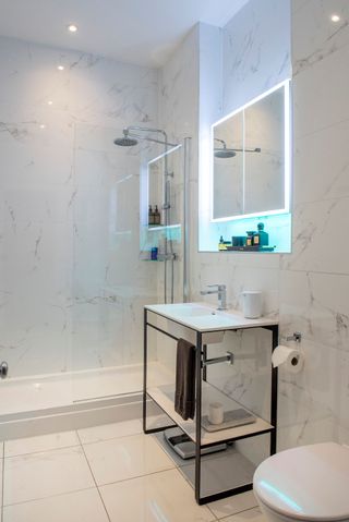 The bathroom has white tiles and a white sink on a stand and a walk-in shower with a mirror next to it