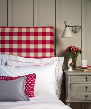 An example of bed ideas showing a headboard in pink gingham fabric with a bunch of flowers on the bedside table