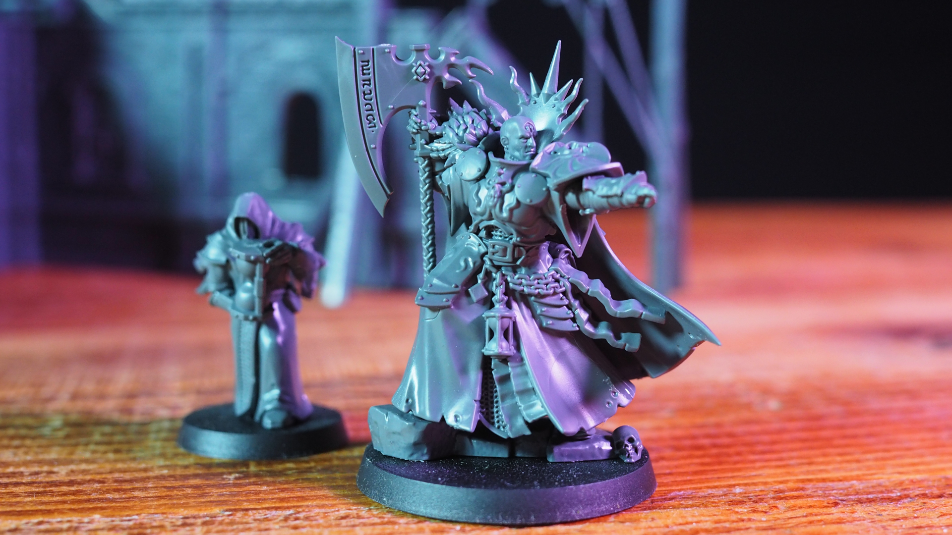 Lord-Terminos model pointing, while a robed figure stands behind them, both on a wooden table