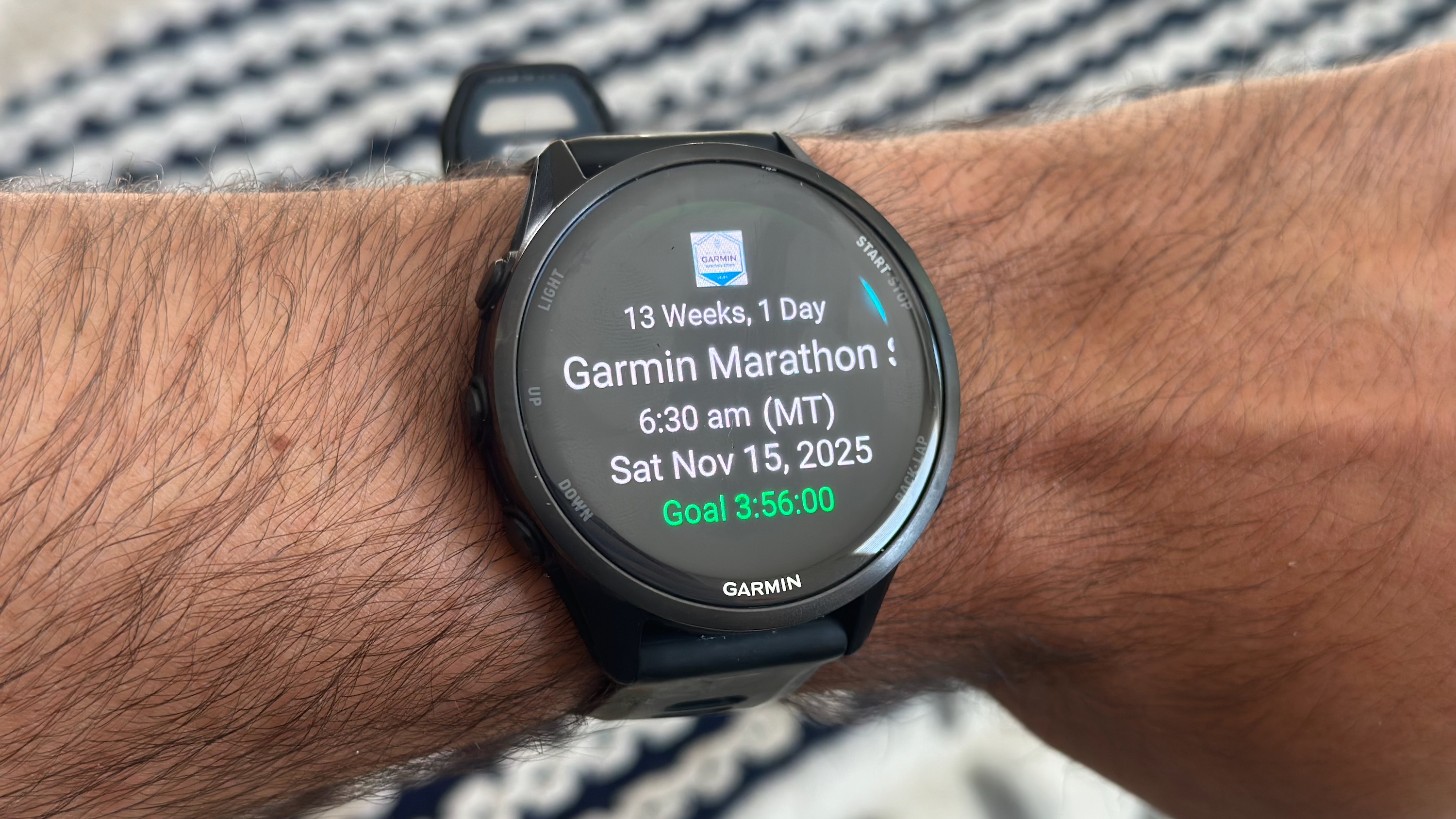 The Garmin Forerunner 970 on the author's wrist, showing the Primary Race widget with the Garmin Tucson Marathon time, date, weeks until the event, and goal time.
