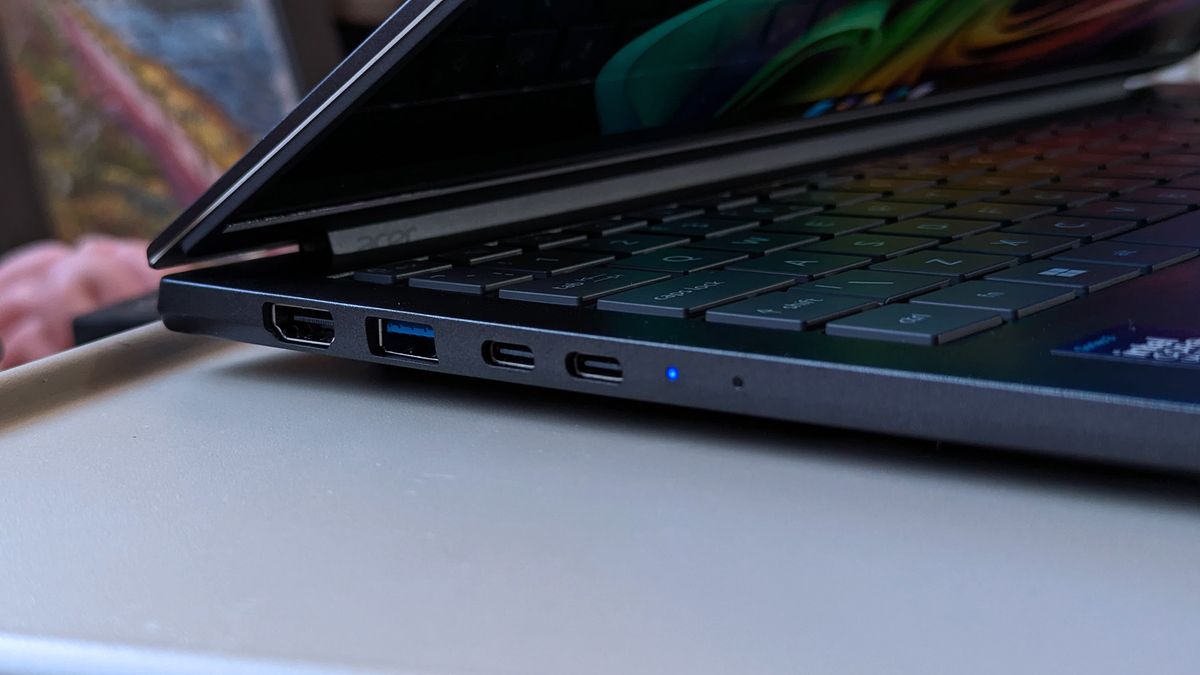 A partially open Acer Swift laptop showing its left-side ports, including HDMI, USB‑A, and dual USB‑C. A blue indicator light glows near the front edge.