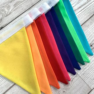 rainbow bunting laying flat on a grey wooden surface, with each of the 10 different coloured triangles slightly visible
