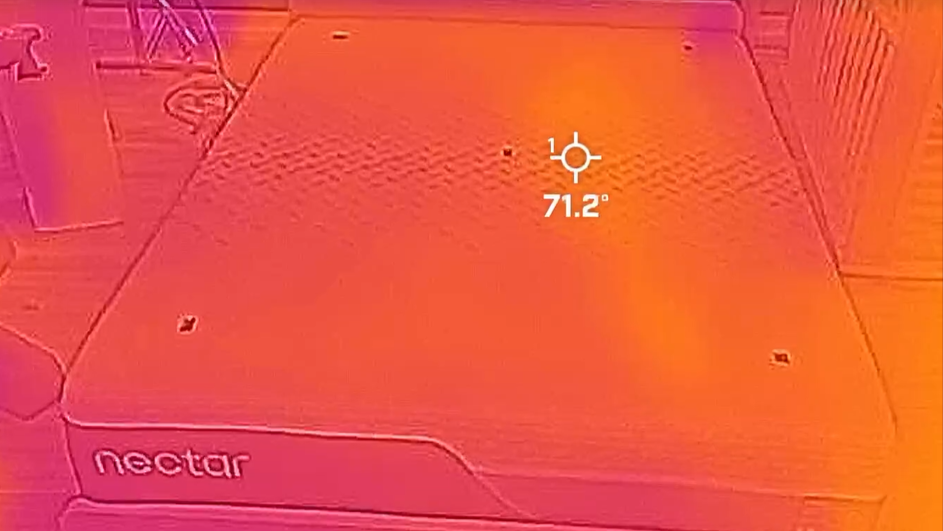A picture of the Nectar Premier Memory Foam Mattress taken with a thermal imaging camera. This image is from after 15 minutes of heat dispersion &mdash; the yellow area stretching across the mattress (contrasted with the purple cooler patches around the room) indicates most of the warmth has left the mattress. However, you can see a faint imprint on the right side of the bed from where our tester, sleep writer Frances Daniels, was lying on the mattress. This shows that the Nectar hasn't completely removed all the warmth it initially absorbed. A target displaying a temperature reading of 71.2&deg;F is placed over the hot spot.
