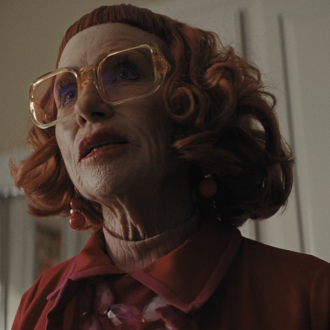 amy madigan as aunt gladys wearing a red jacket and big clear glasses in a still from weapons