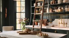 Dark green pantry with wall storage with different size jars and a freestanding island with a marble top