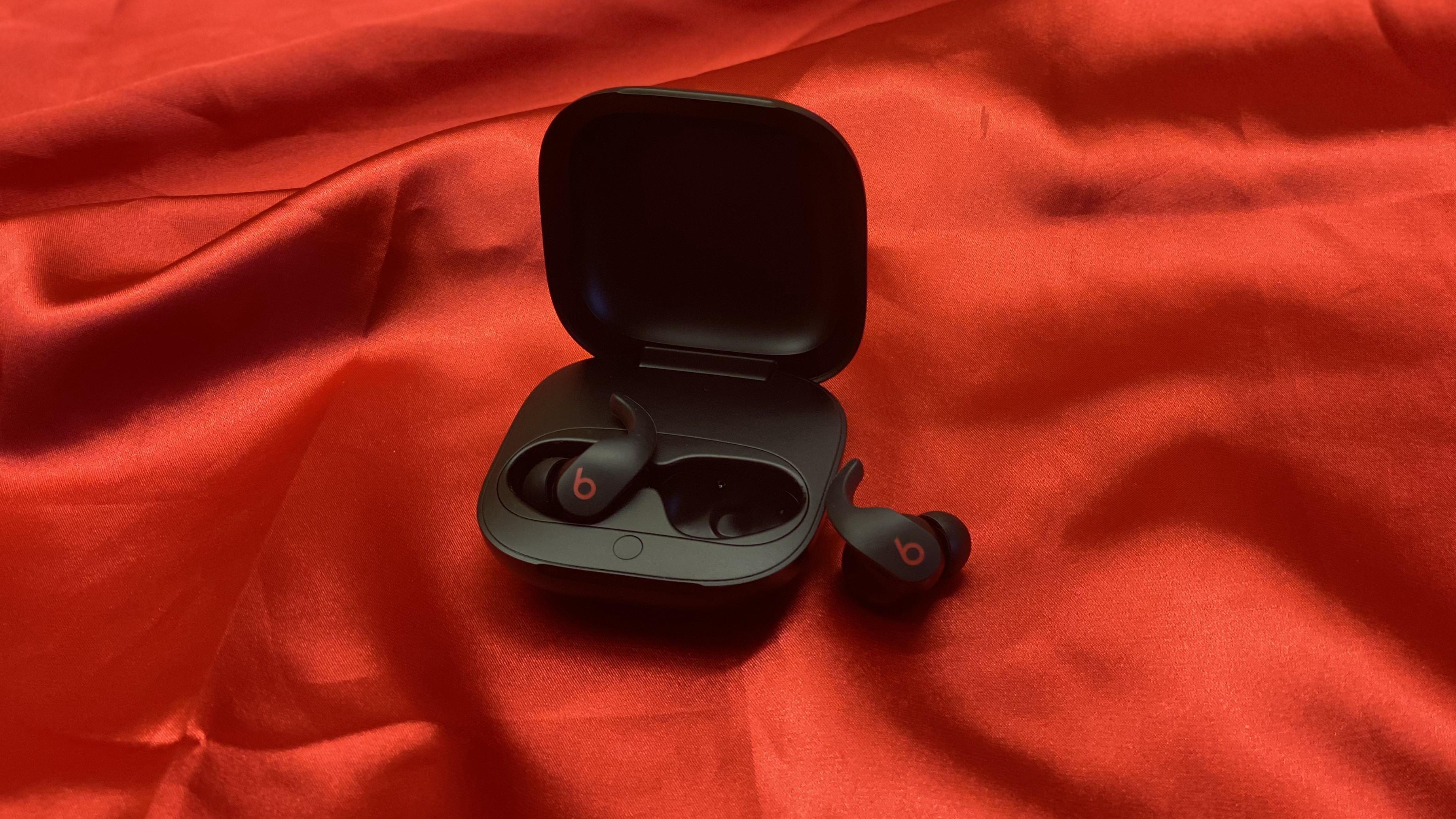 Los earbuds Beats Fit Pro true wireless en su estuche de carga sobre fondo rojo