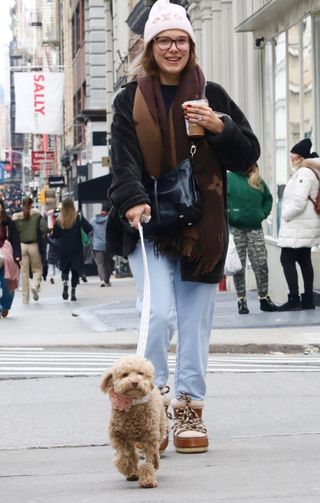 Millie Bobby Brown matches her poodle in a black teddy coat jeans and Chloe moon boots while walking in SoHo