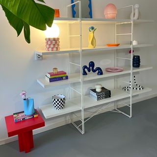 A white shelving unit displaying decorative items next to a red-painted IKEA side table with an updated base