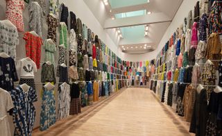 A wall of hanging garments lines the walls of the gallery
