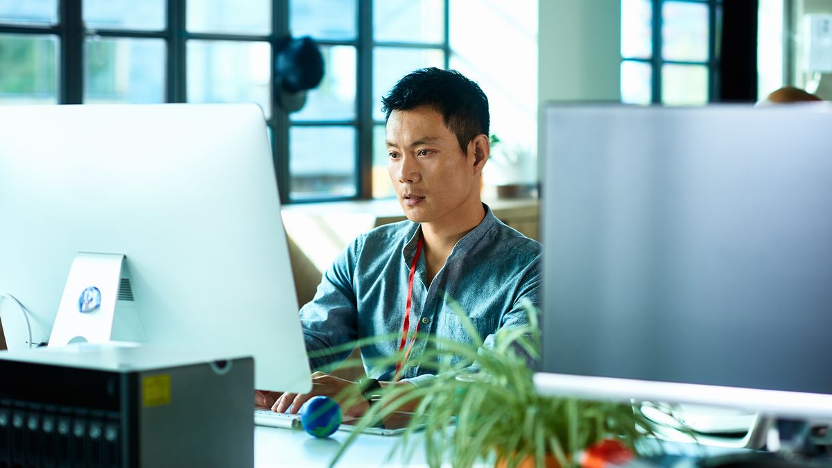 Office worker working on a desktop computer using applications in an open plan office space.