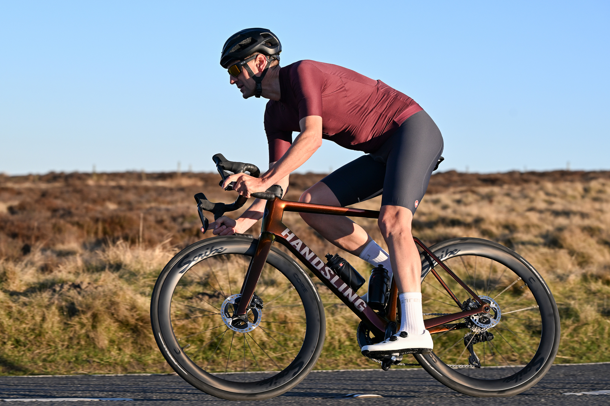 Man wearing a burgundy jersey riding a Handsling bike with Scribe wheels on a moorland road