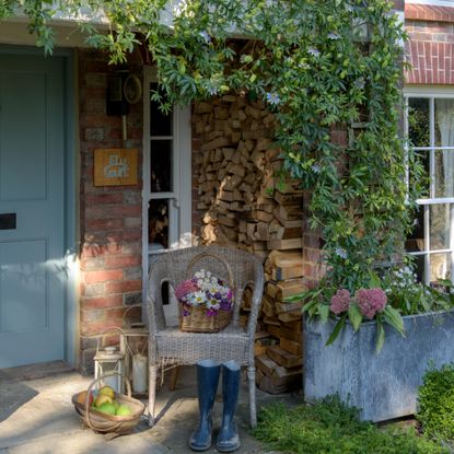A front porch with an outdoor wicker chair with a basket of flowers on top and a blue front door