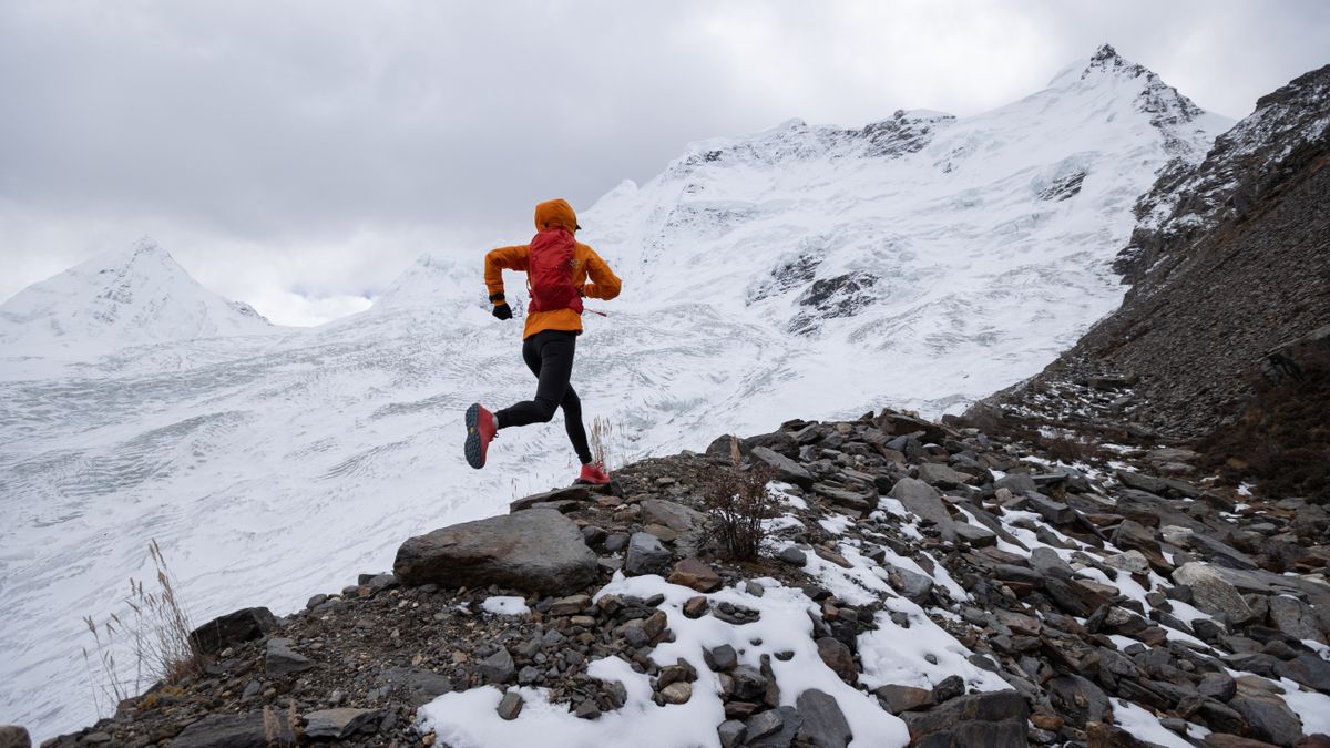 Woman trail runner cross country running up hill to winter snow mountain top