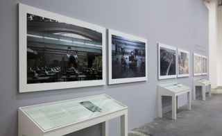 Six landscape photos displayed on a wall, the first two showing two people in a warehouse.