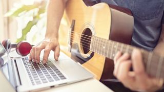 Close up of acoustic guitar playing taking lessons on his laptop