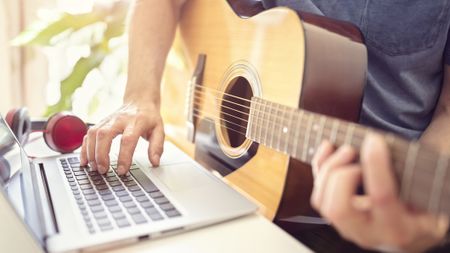 Close up of acoustic guitar playing taking lessons on his laptop