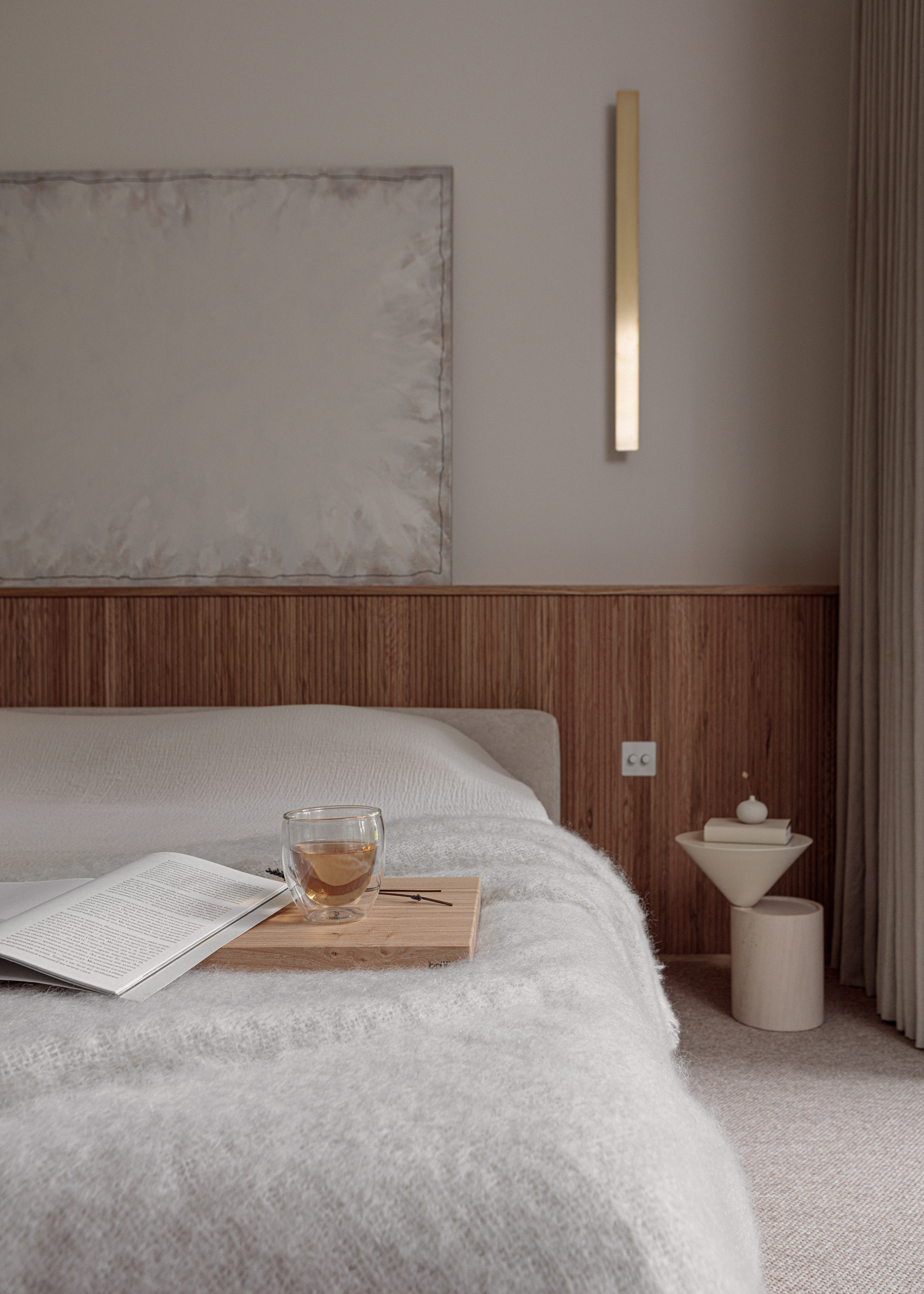 A cozy bedroom with a white bed featuring a fuzzy throw and a tray with a glass of tea and a book