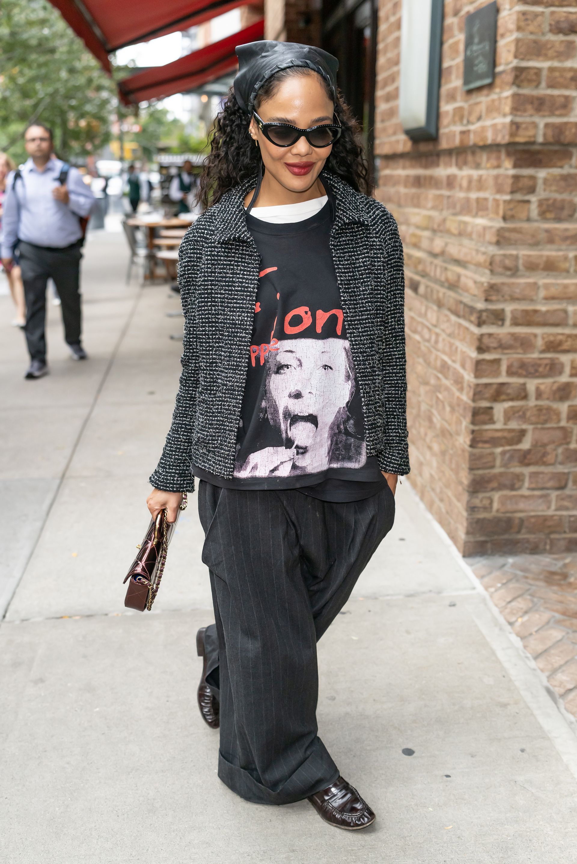 Tessa Thompson wearing a Chanel tweed jacket, gray striped pants, a graphic t-shirt, and black loafers