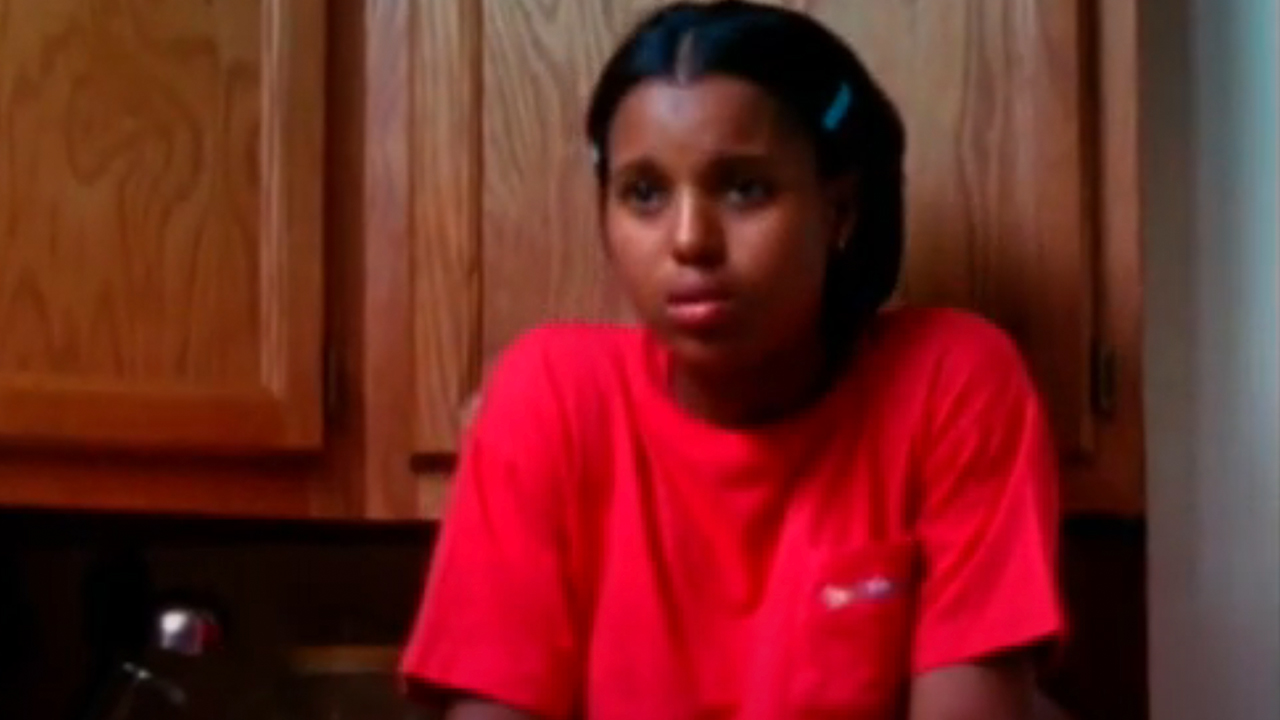 Kerry Washington wearing a red shirt, sitting in front of a cabinet in Our Song