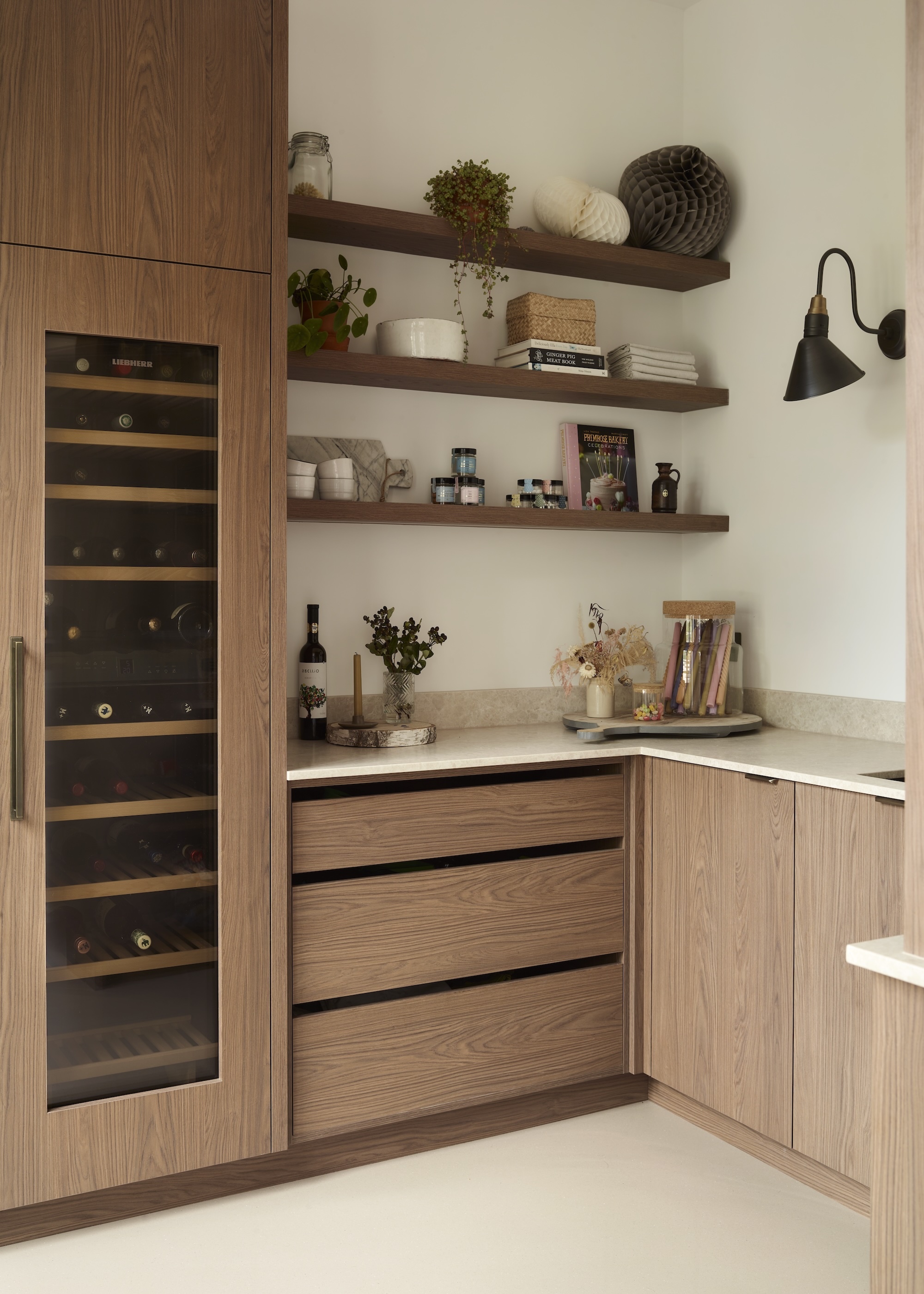 A mid toned timber, handle-free kitchen showing a corner zone with drawers and a wine cabinet