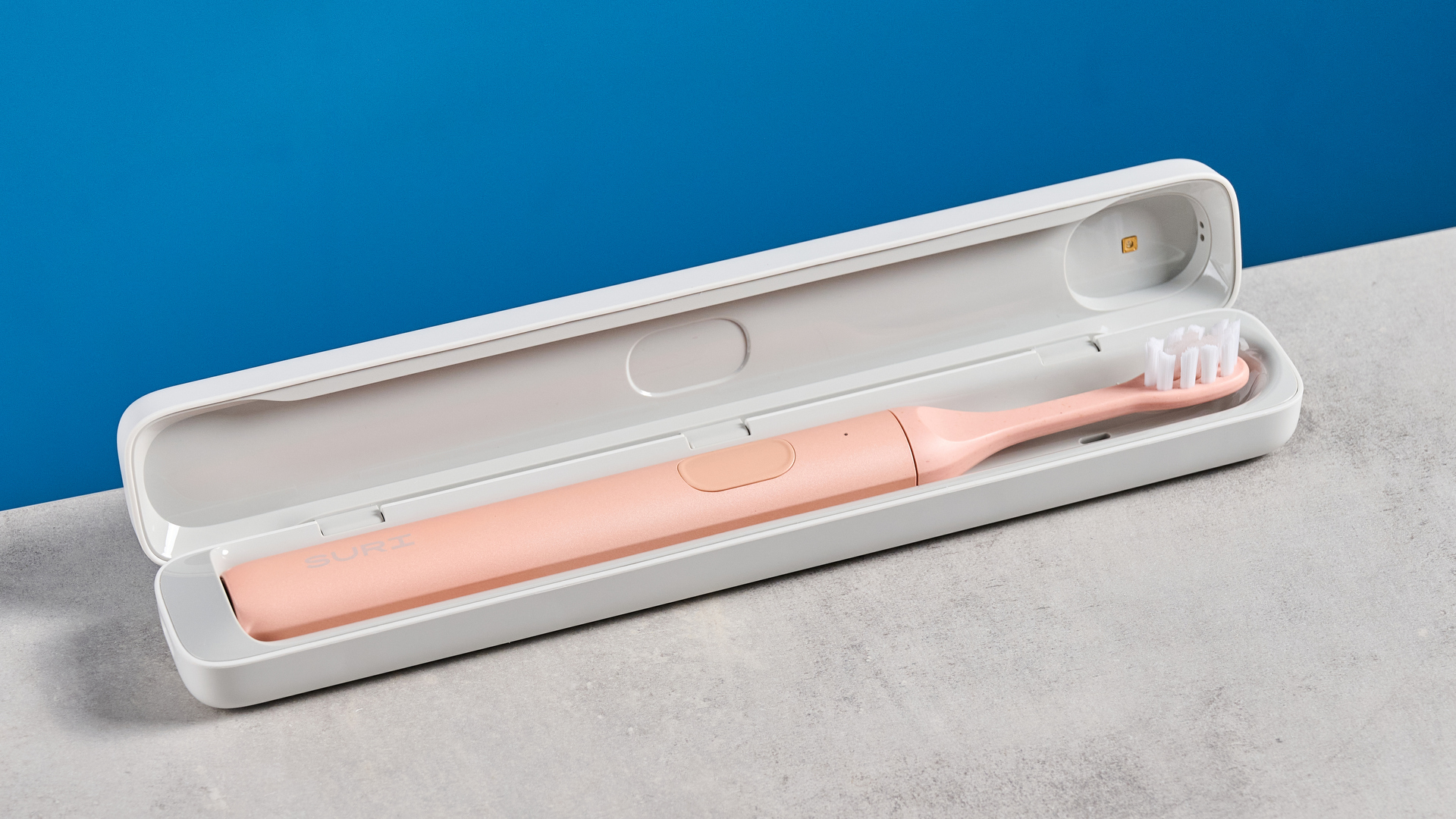 the Suri 2.0 toothbrush in sunset bloom pink colorway with a plant-based head and aluminum body, pictured with its uv cleaning travel case and the suri toothpaste