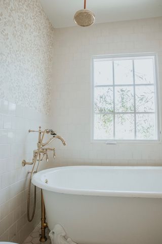 Neutral colored tiled bathroom with gold faucets on white bathtub