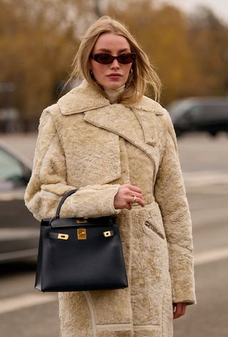 a street-style photo of a woman wearing an Hermés bag with a shearling coat in a story about how to buy an hermés bag