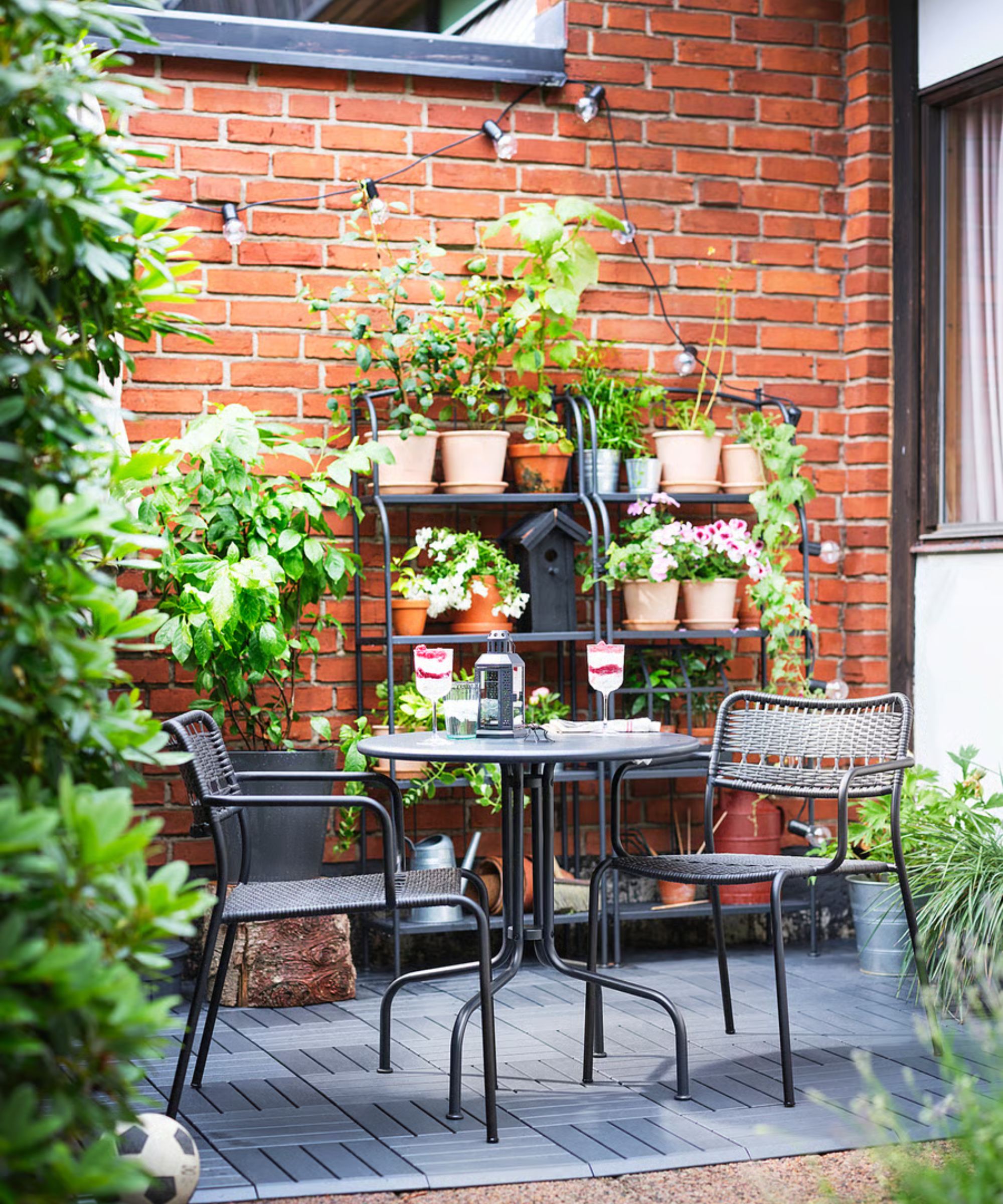an outdoor dining set up with two chairs, a table, and two shelves in the background holding plants