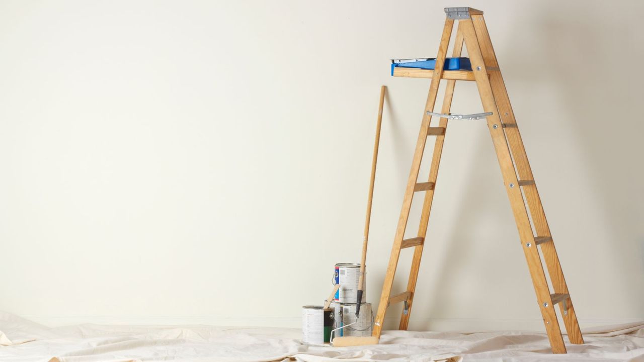 Ladder in a room in front of a black wall with some painting tools