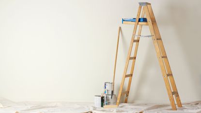 Ladder in a room in front of a black wall with some painting tools