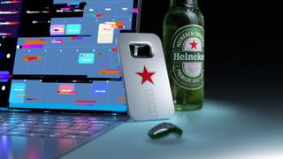 Heineken's 'The Closer' bottle opener leaning against a bottle of Heineken lager, in front of open laptop showing coloured spreadsheet