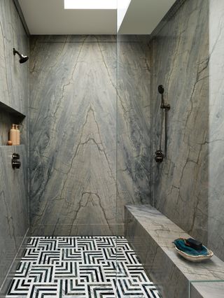 A dark grey bookmatched slab shower with black and white patterned floor tiles