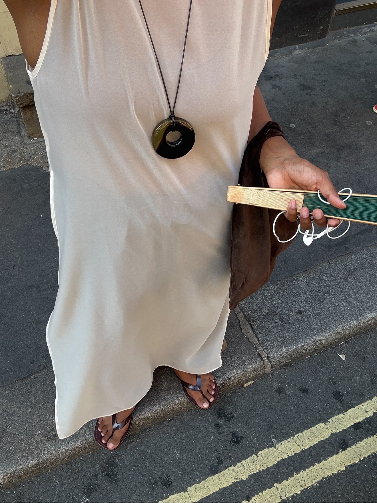 A woman taking a picture of her outfit wearing brown flip flops with a natural-looking pedicure