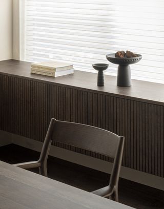 A chair and dining table placed in front of a built in cabinet by a window