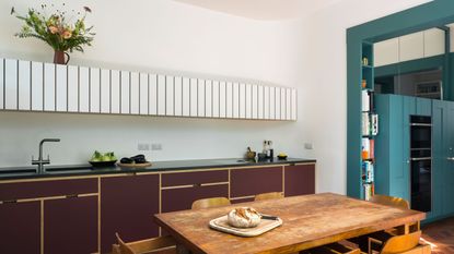 Uncommon Projects kitchen in the Blue House, Hackney. Blue door frame and cabinets, burgundy cabinetry, white panelled upper cabinets, timber dining table with chairs